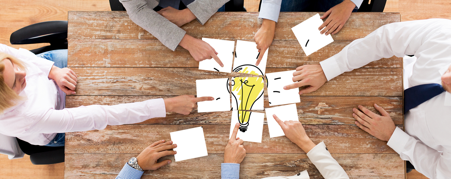 close up of creative team sitting at table and putting together puzzle pieces with light bulb picture